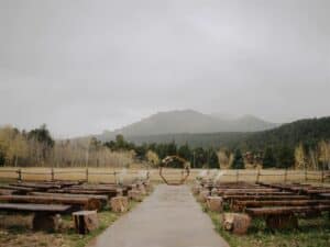 a ceremony site full of wooden benches and a beautiful wooden arch sit at the base of a mountain on a foggy day at wild basin lodge before a wedding ceremony