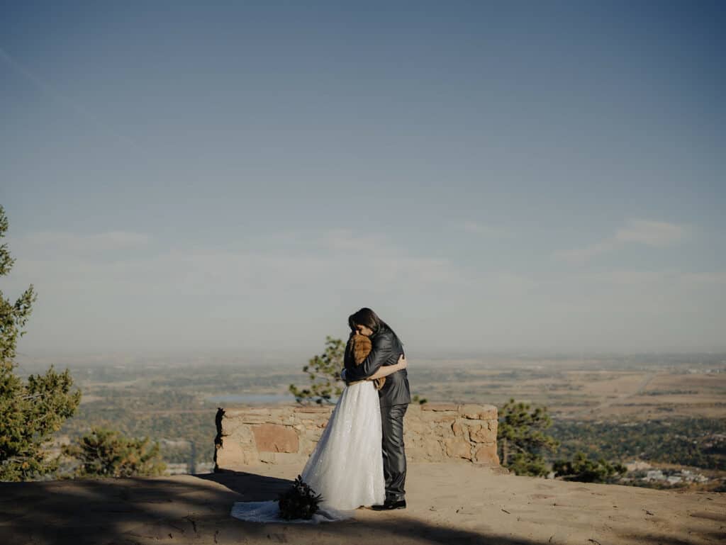 a bride and groom embrace overlooking boulder at sunrise amphitheater