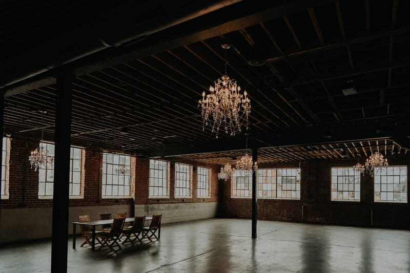 Colorado wedding venue Moss Denver is shown showcasing the chandelier room with floor-to-ceiling windows and a hanging chandelier