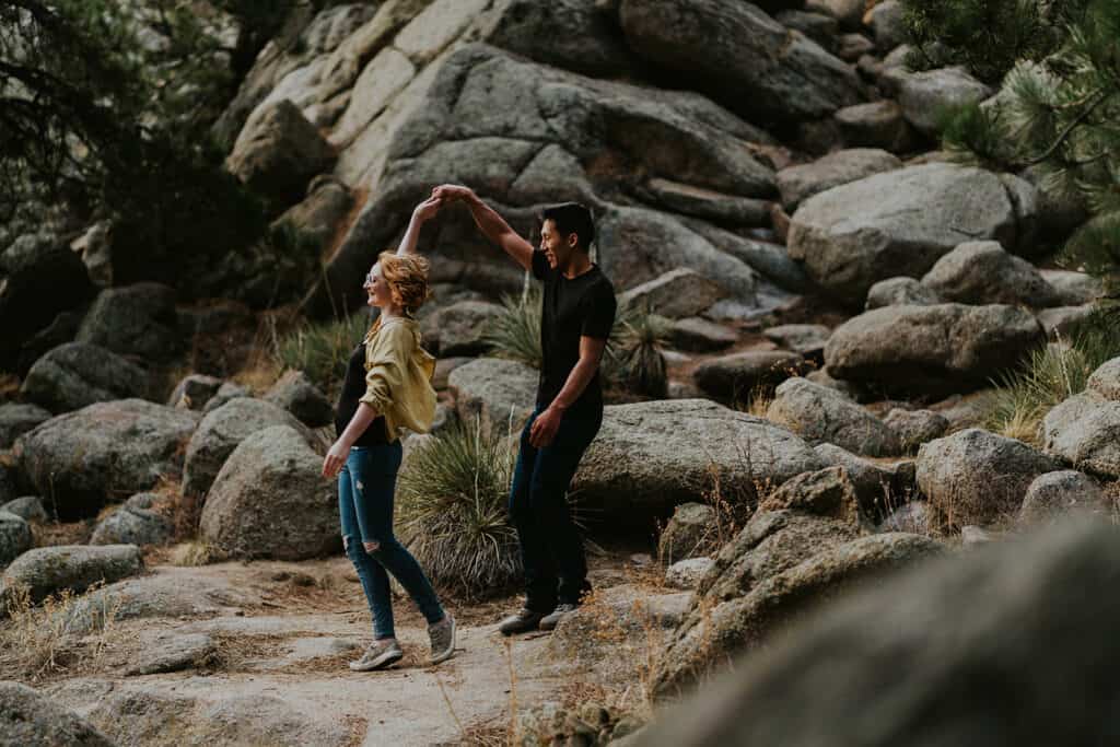 a couple dances in front of a rocky slope on flagstaff mountain for their boulder engagement session photographed by Alex medvick