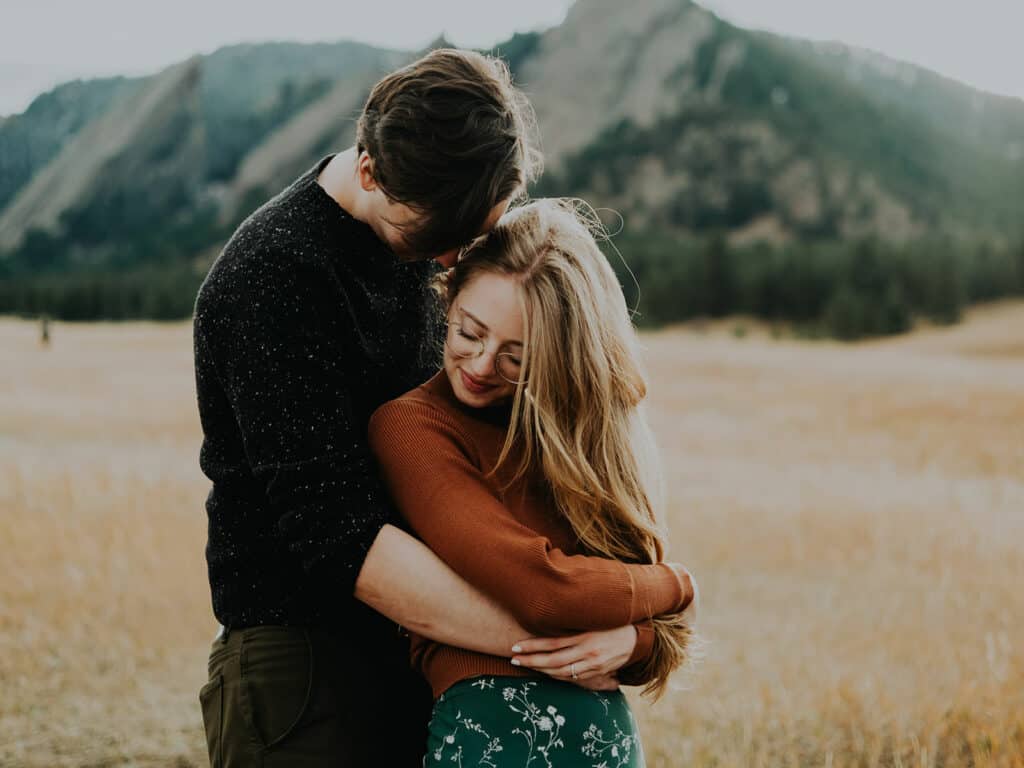 man in black sweater embraces girl in orange sweater in Chautauqua park in boulder Colorado for their engagment photos by Alex Medvick