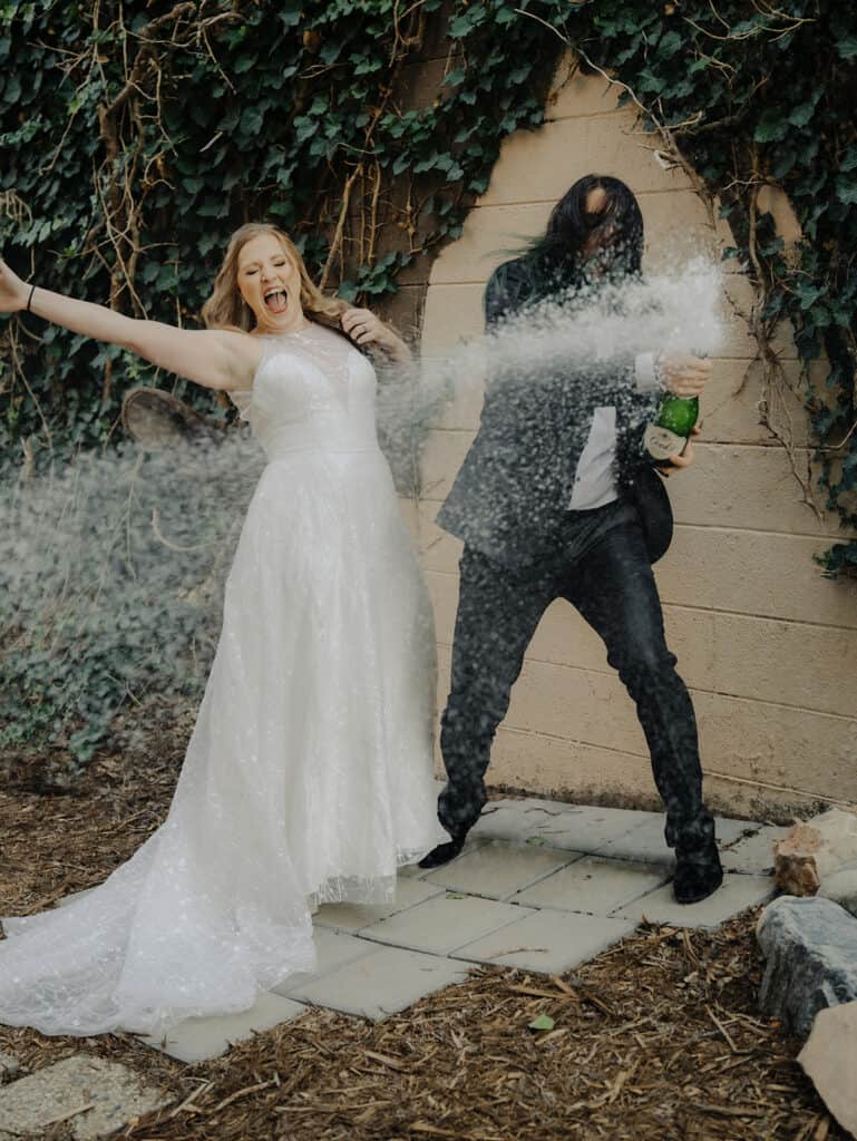 a bride and groom spray champagne in the outdoor cocktail courtyard of Rembrandt Yard in Boulder Colorado 